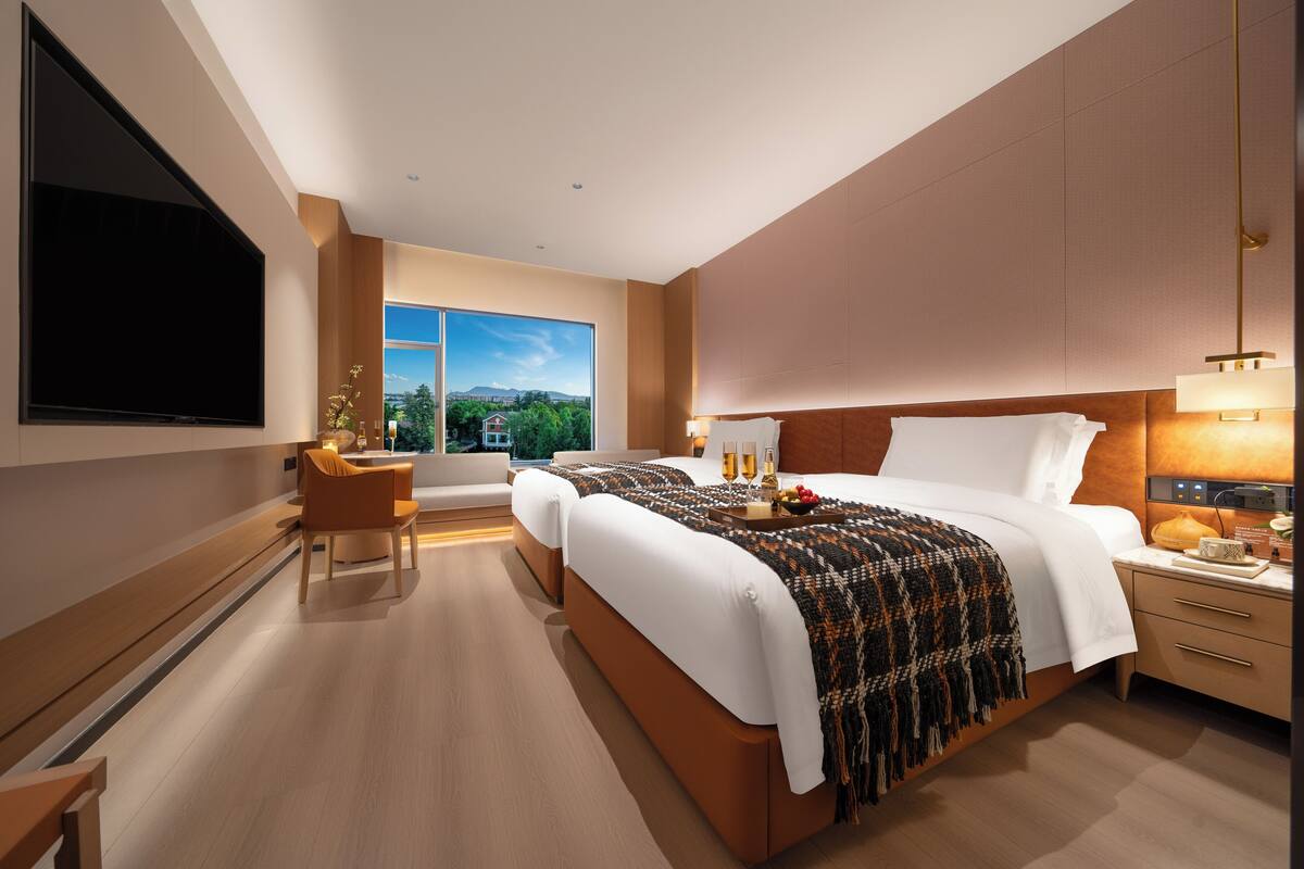 A modern hotel room with a large bed, a TV, a seating area, and a view of the outdoors.