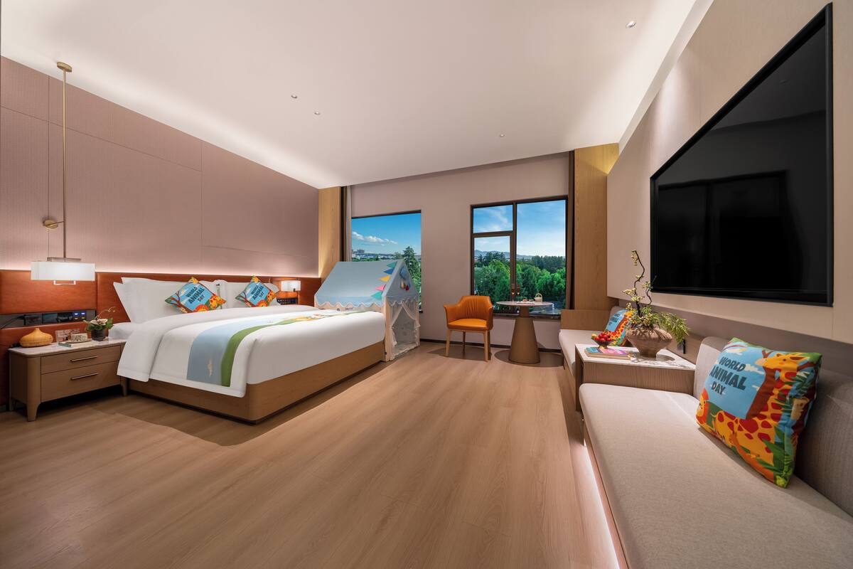 A modern hotel room with a large bed, a sofa, a desk, and a view of the outdoors.