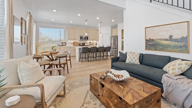 A spacious living area with a sofa, coffee table, and dining table. A kitchen with modern appliances and bar stools is visible in the background. - Ski Basecamp • Cozy Modern • Minutes to Everything (Midvale)