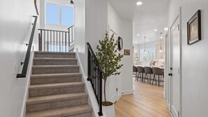A staircase with a potted plant, a dining area with bar stools, and a kitchen in the background. - Ski Basecamp • Cozy Modern • Minutes to Everything (Midvale)