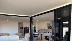 Una sala de estar moderna con un amplio sofá modular en forma de L, un cofre de madera y una zona de comedor con mesa y sillas.