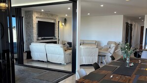 Una sala moderna con un televisor grande, asientos cómodos y un comedor con una mesa y sillas de madera.
