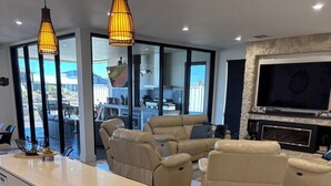 Una sala de estar moderna con un sofá en forma de L grande, una isla de cocina integrada y un televisor de pantalla plana montado en una pared de piedra.