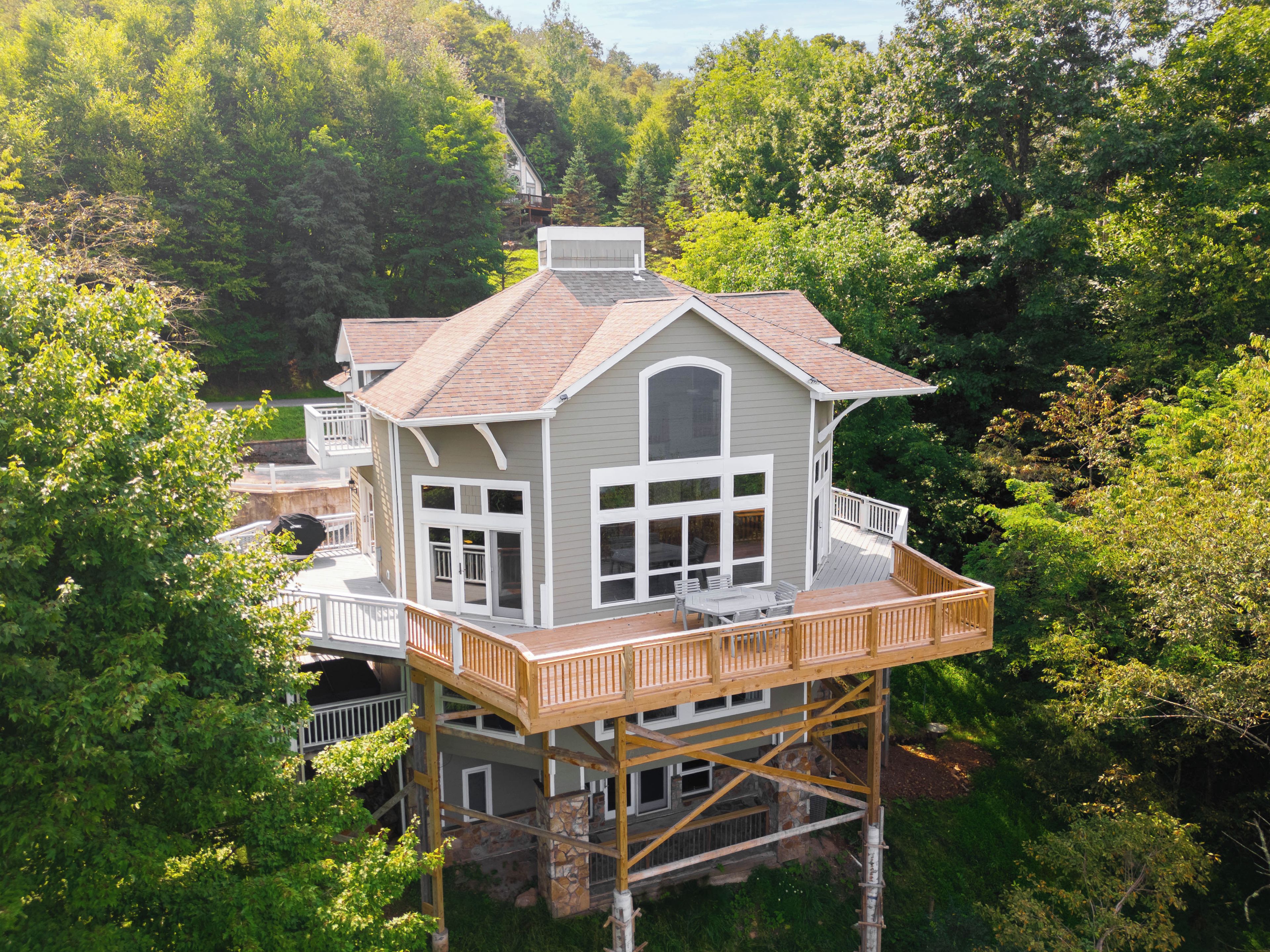A multi-story house with a deck, surrounded by dense forest.