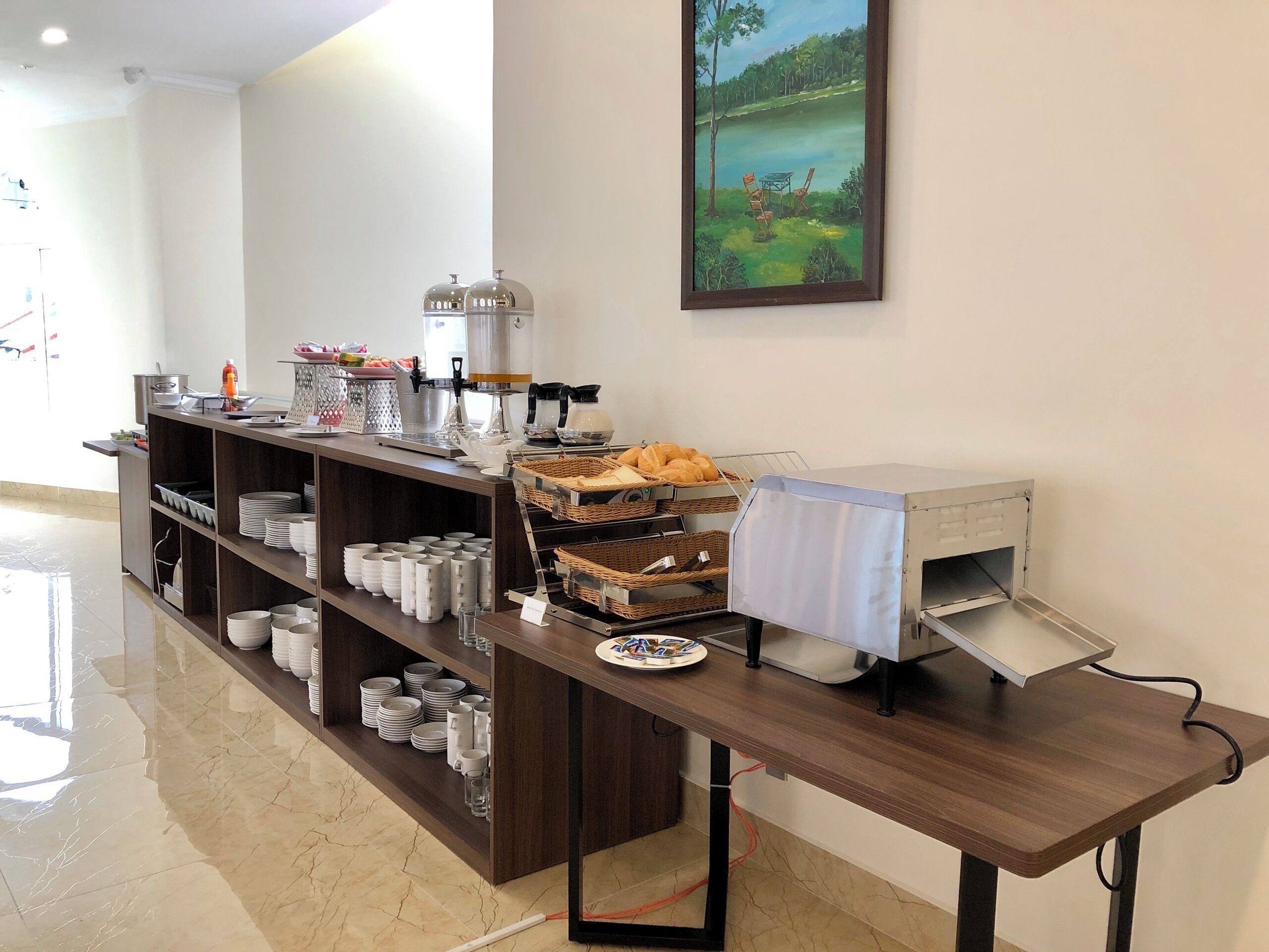 Un'area buffet con diversi cibi e utensili, una macchina per il caffè e un quadro appeso al muro.