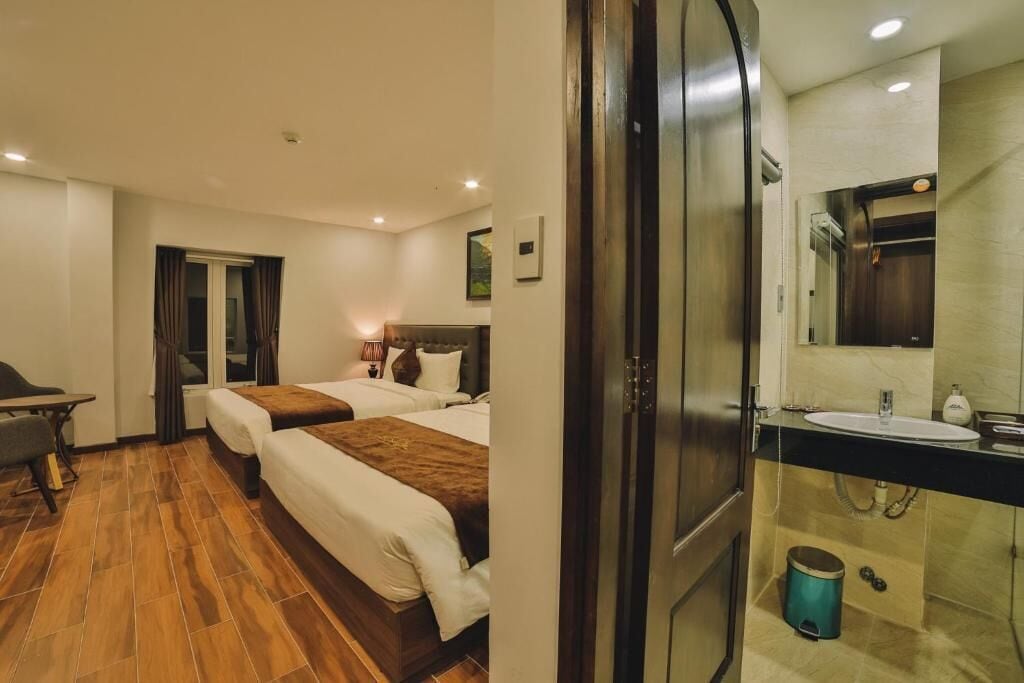 A hotel room with two beds, a desk, a bathroom with a sink and mirror, and a wooden floor.