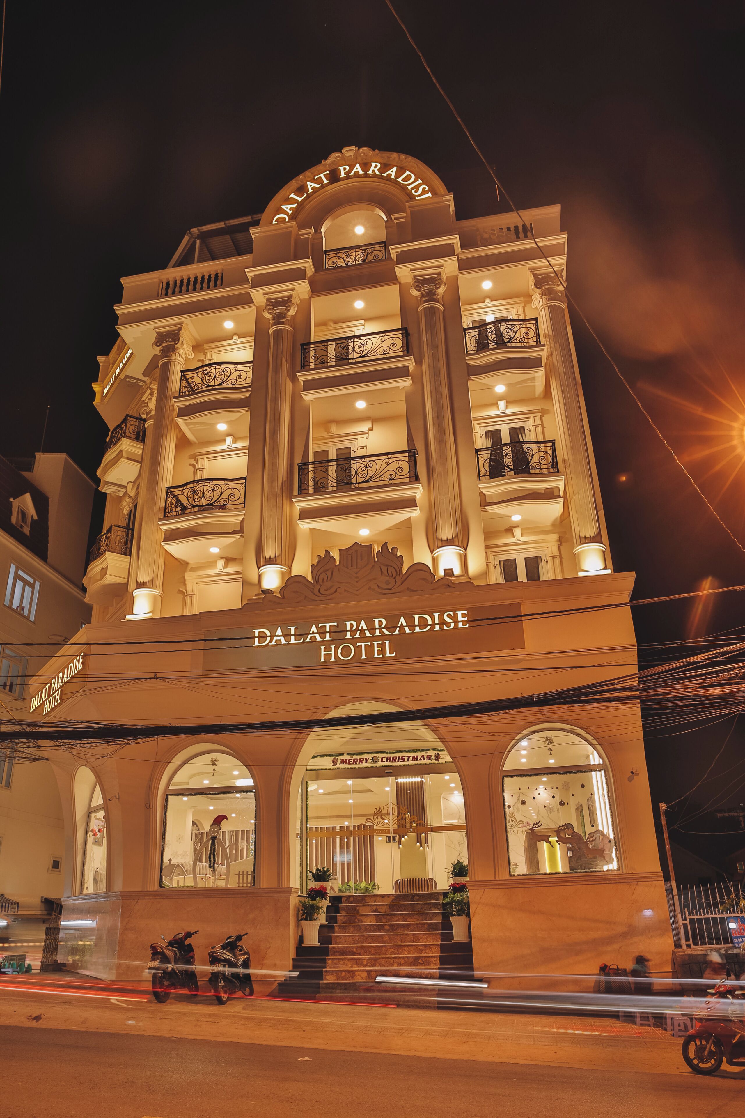 The exterior of Dalat Paradise Hotel with a prominent sign, multiple balconies, and a staircase leading to the entrance.