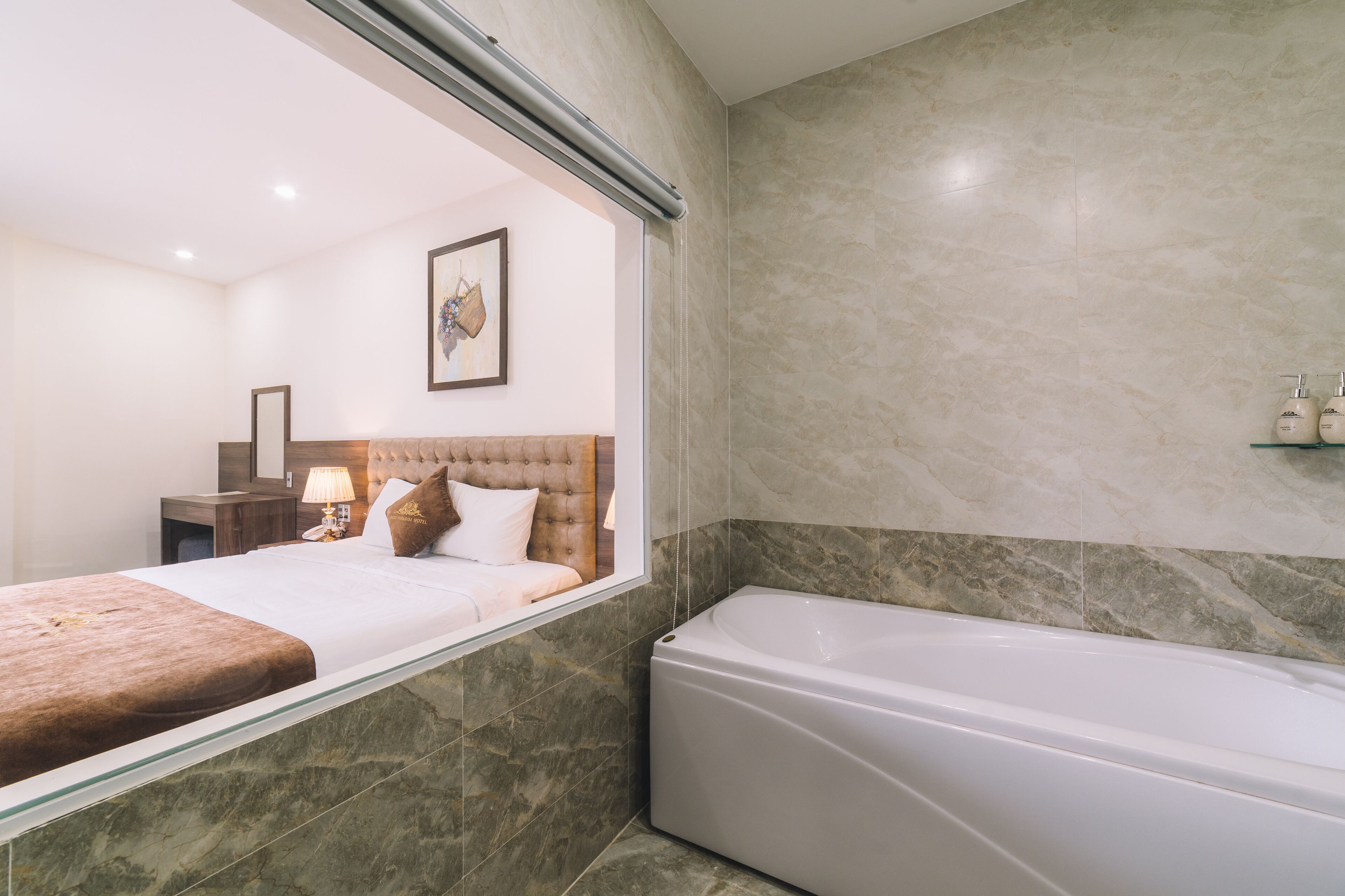 A modern bathroom with a large bathtub, a bed with a brown headboard, and a framed picture on the wall.