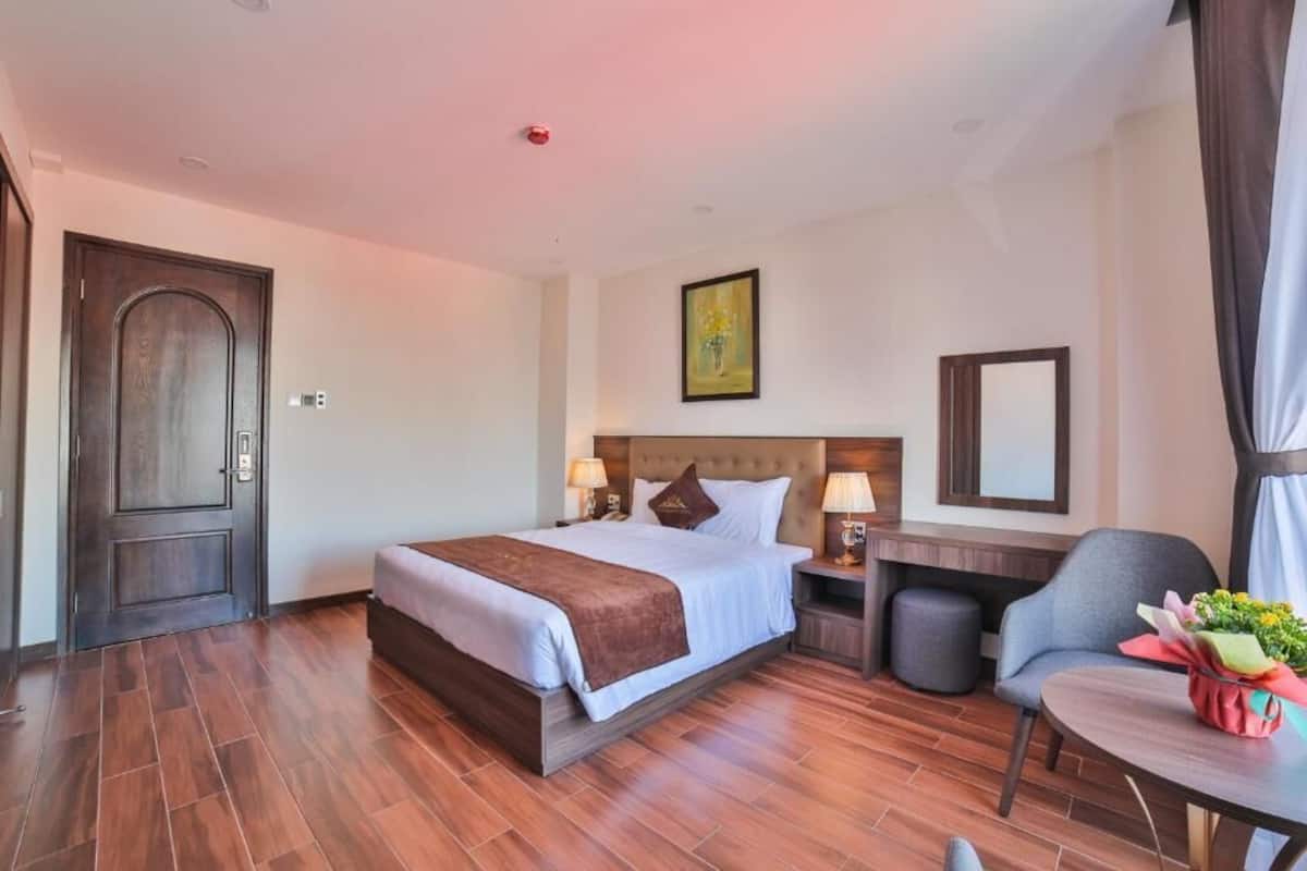 A hotel room with a large bed, bedside tables, a desk, a chair, and a small table with a vase of flowers.
