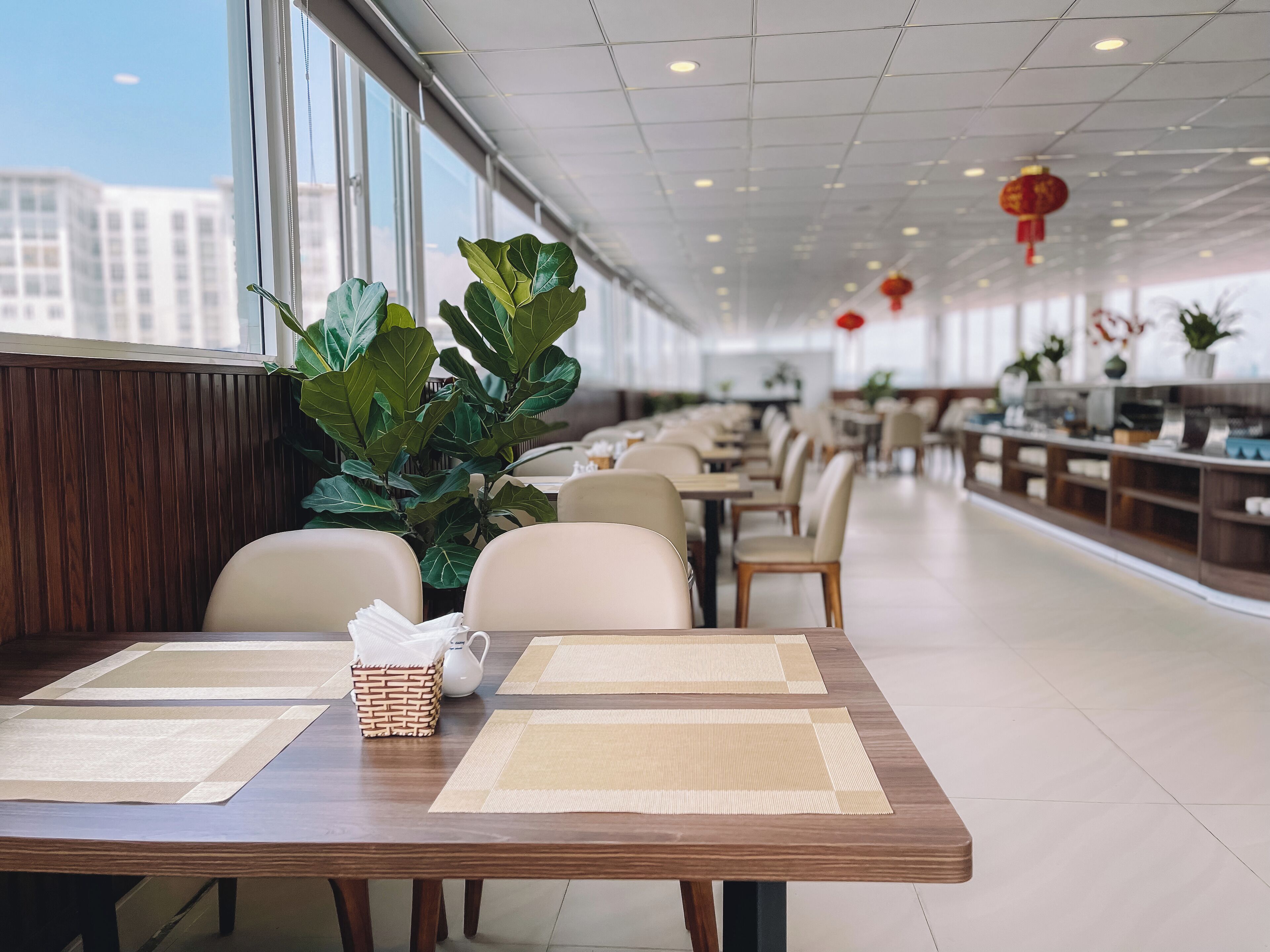A spacious dining area with long tables, chairs, and potted plants.