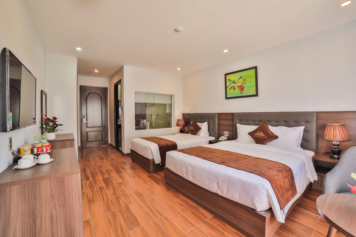 A hotel room with two beds, a desk with a mirror, a TV, and a bathroom visible through a glass door.