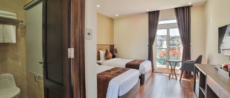 Camera d'albergo con due letti, una scrivania, una sedia, un bagno e un balcone con vista.