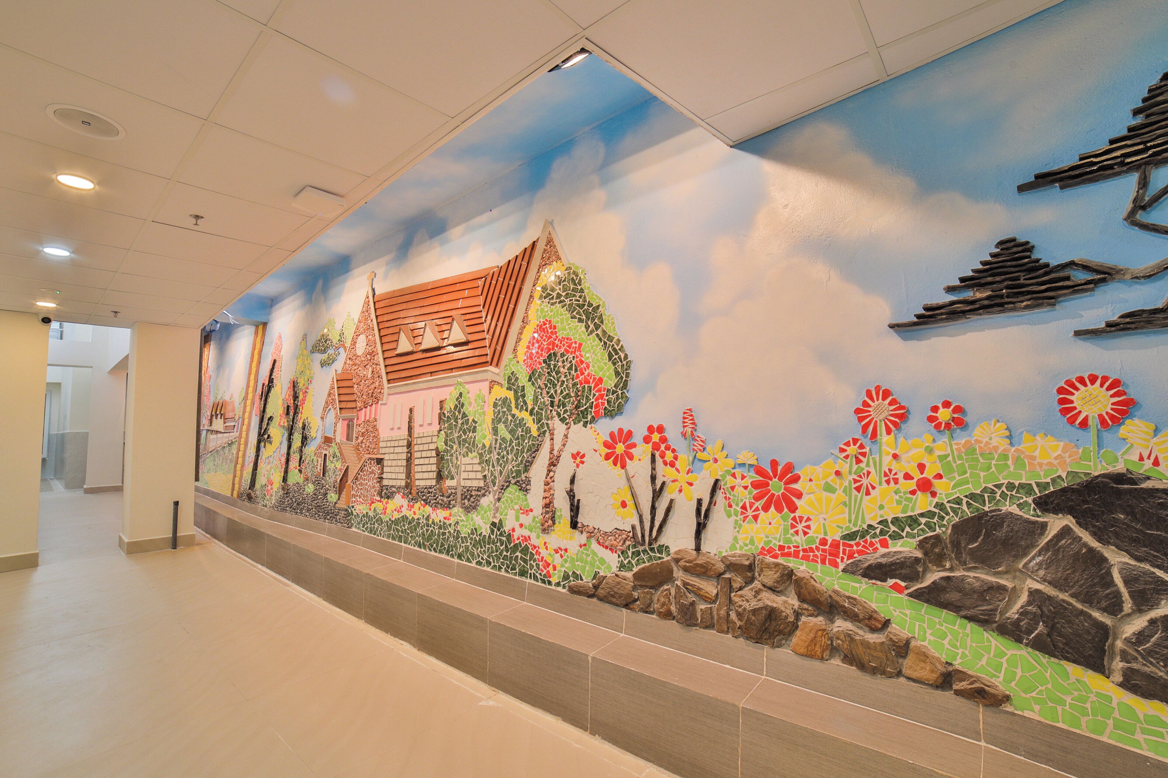 Un pasillo decorado con un mural de colores que representa una construcción tradicional, árboles y flores.