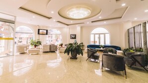 Un hall d’entrée spacieux, agrémenté d’un lustre, d’un coin salon et de grandes fenêtres.