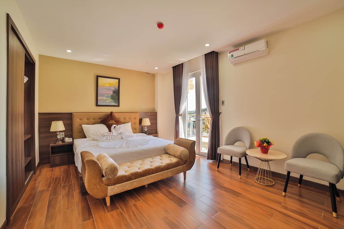 A hotel room with a large bed, a sofa, two armchairs, a small table, and a balcony with curtains.