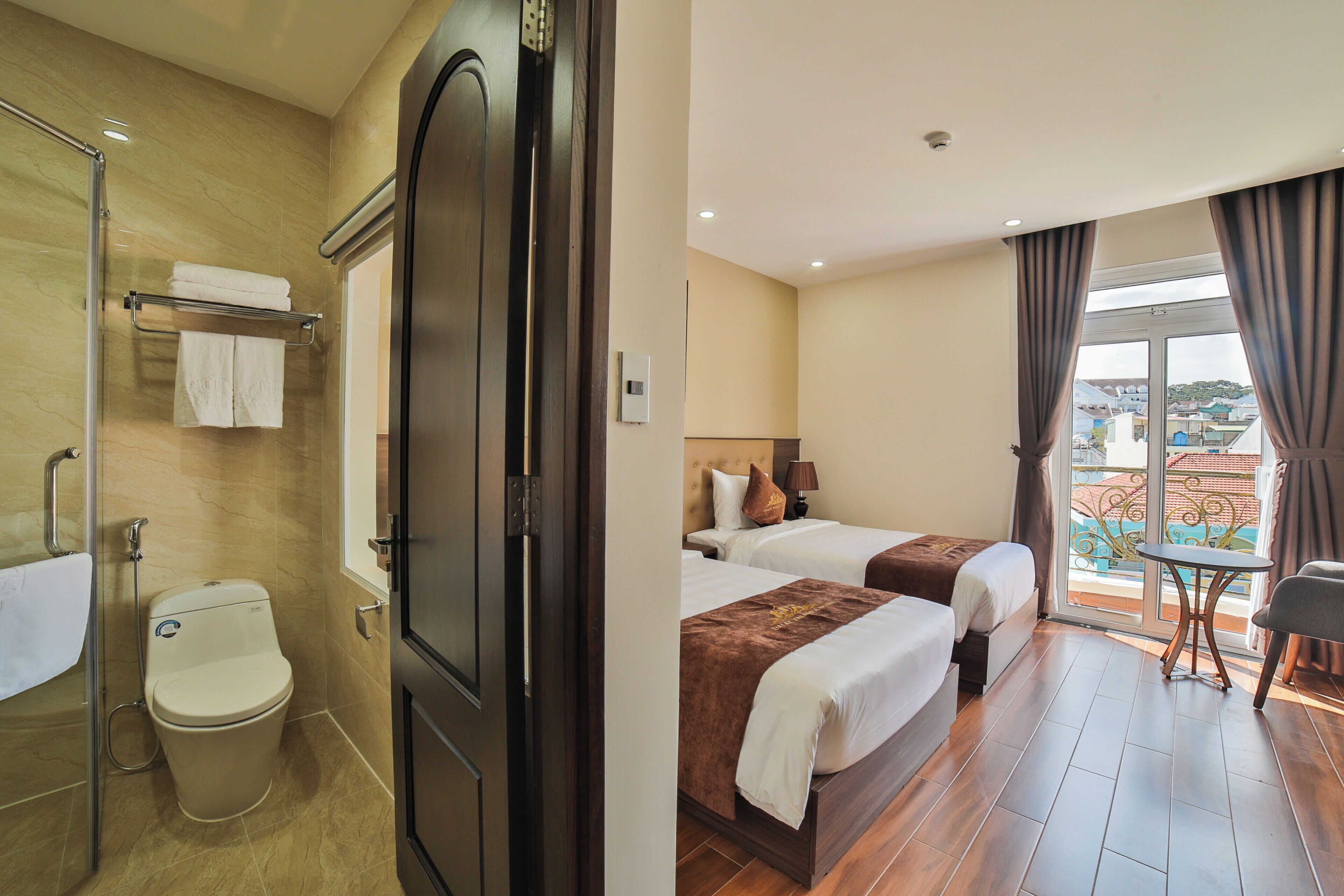 A hotel room with a bathroom, two beds, a balcony, and a view of the city.