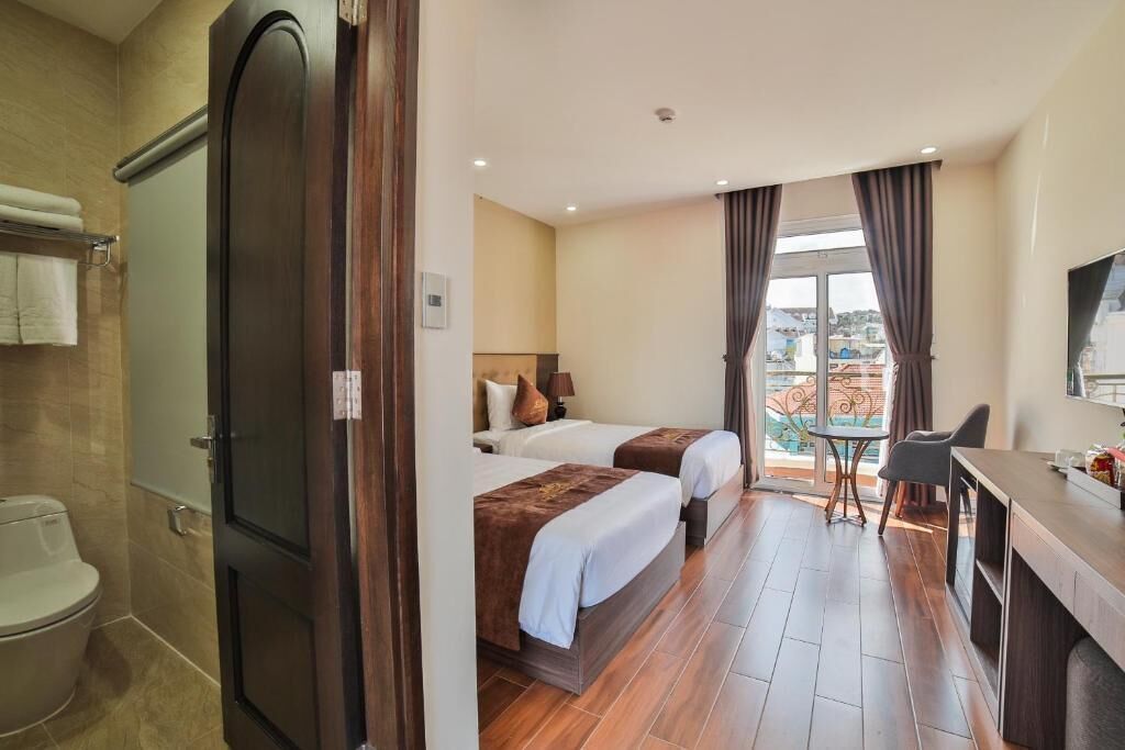 Ein Hotelzimmer mit zwei Betten, einem Schreibtisch, einem Stuhl, einem Balkon und Blick auf die Stadt.
