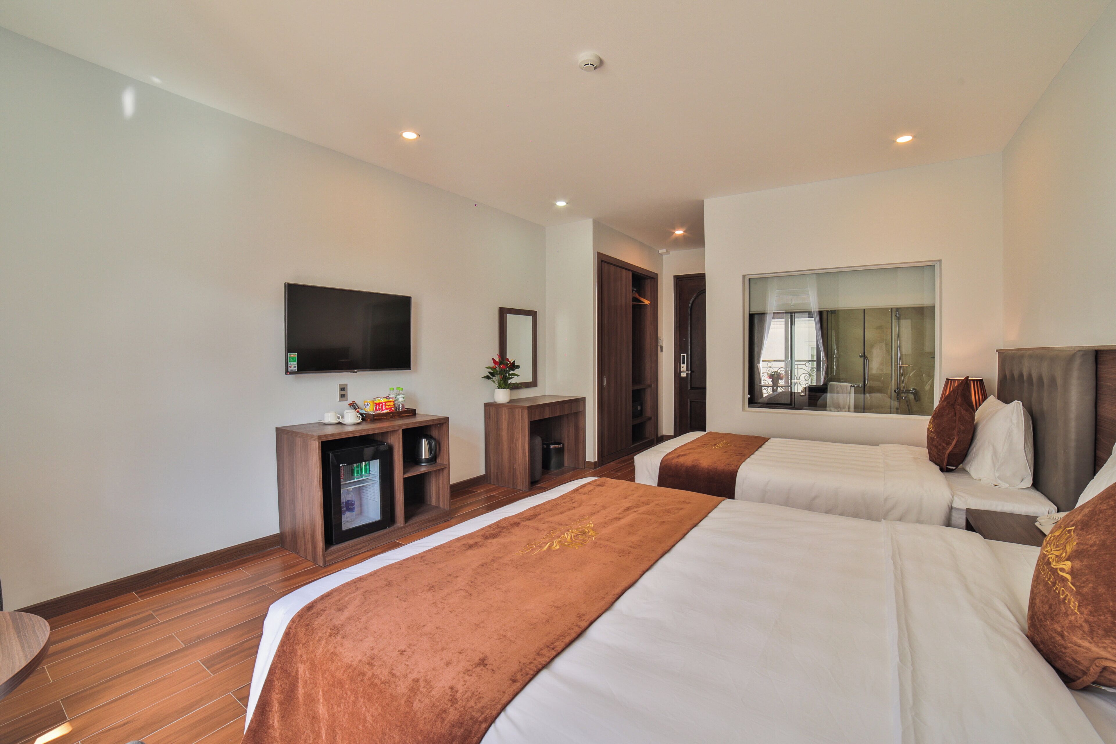 A hotel room with two beds, a TV, a minibar, and a large window.