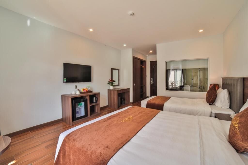 A hotel room with two beds, a TV, a minibar, a mirror, and a window with a view.