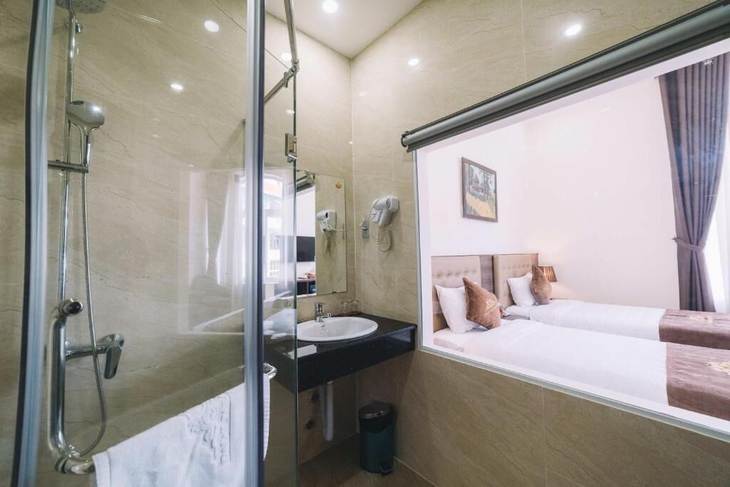 A hotel room with a glass shower enclosure, a sink, a hairdryer, and a bed with a headboard.