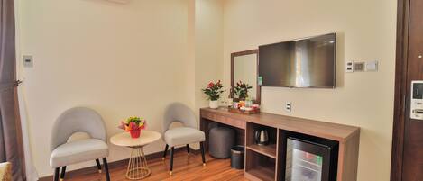 A modern room with a wooden floor, two grey armchairs, a small round table, a built-in TV, and a mini-fridge.