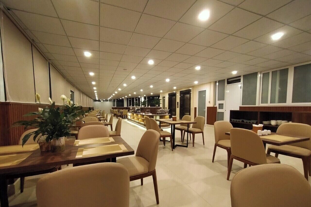 A long corridor with tables and chairs, a counter with a display, and a plant.