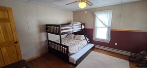 Een stapelbed in een kamer met een houten deur, een raam met gordijnen en een plafondventilator.