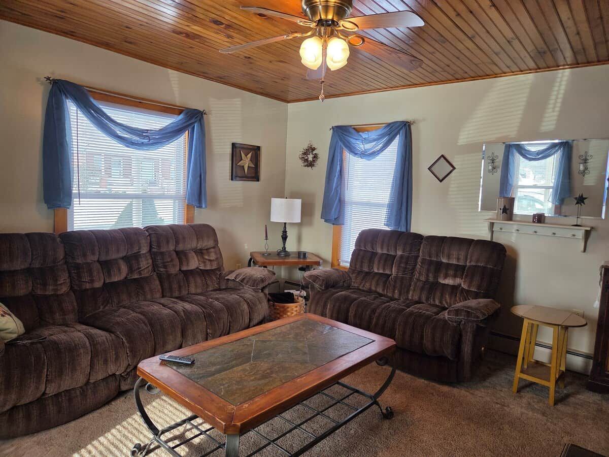 A cozy living room with a sectional sofa, a coffee table, and a ceiling fan.