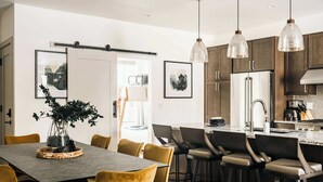 Ett modernt kök med en central köksö, hängande lampor och en matplats med bord och stolar.