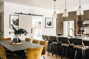Eine moderne Küche mit einer zentralen Kochinsel, Pendelleuchten und einem Essbereich mit Tisch und Stühlen.
