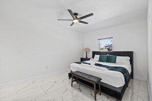 A hotel room with a bed, a bench, a ceiling fan, a nightstand, and a window. - The Bradenton Estate: Pool, Pickleball, Mini-Golf & Jacuzzi (Bradenton)