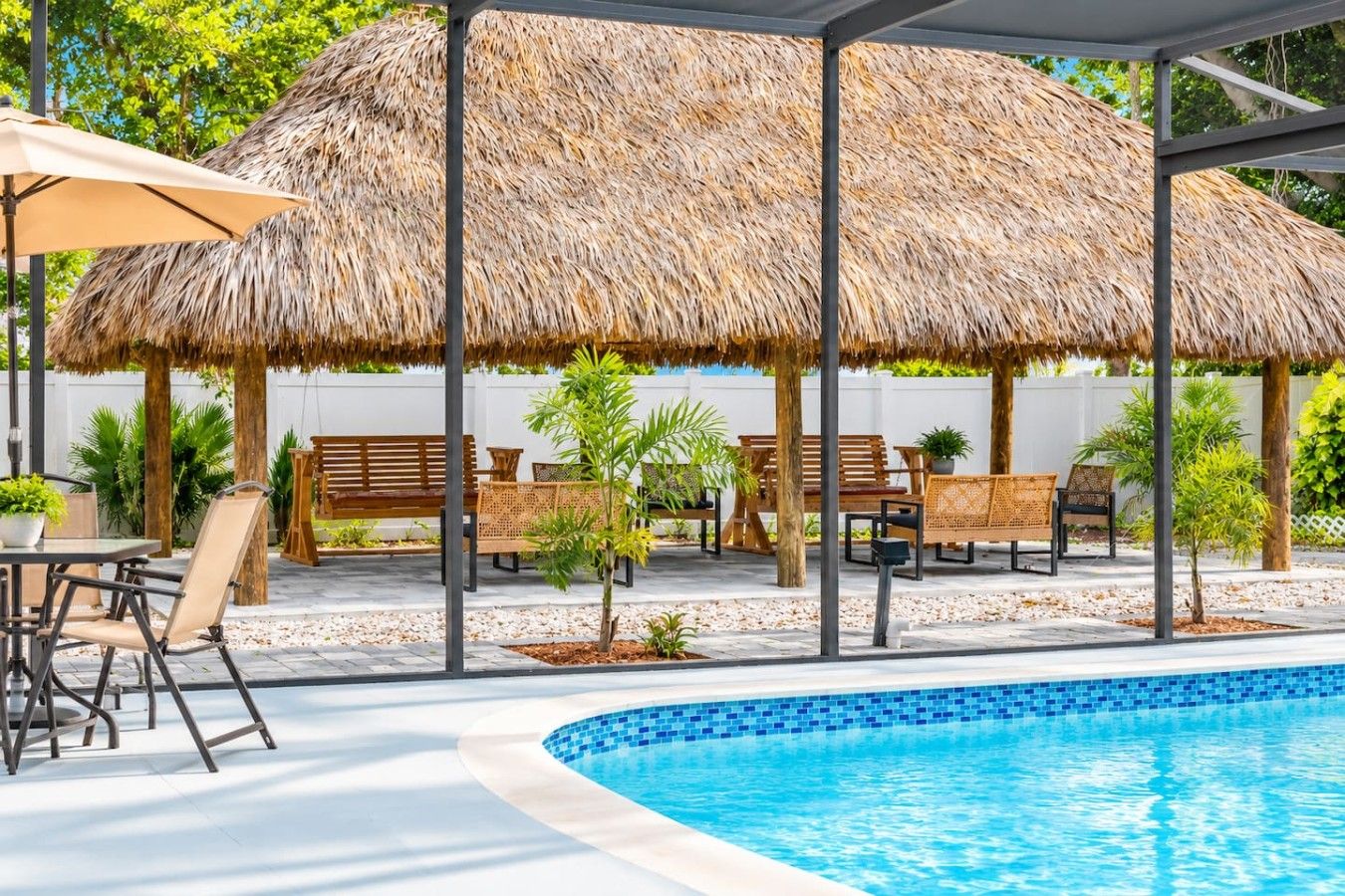 A pool area with a thatched roof structure, outdoor seating, and a clear blue pool.