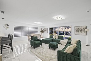 A modern living room with a dining area, large windows, and a view of the outdoors. - The Bradenton Estate: Pool, Pickleball, Mini-Golf & Jacuzzi (Bradenton)