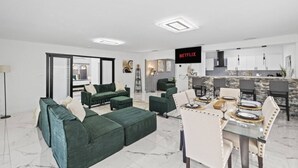 En moderne stue med sofaarrangement, et spiseområde med et glasbord og et køkken med stenbeklædt bagvæg.