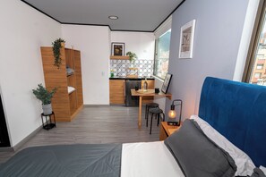 Une chambre d’hôtel compacte comprenant un lit, un bureau avec une chaise, une kitchenette et une grande fenêtre.