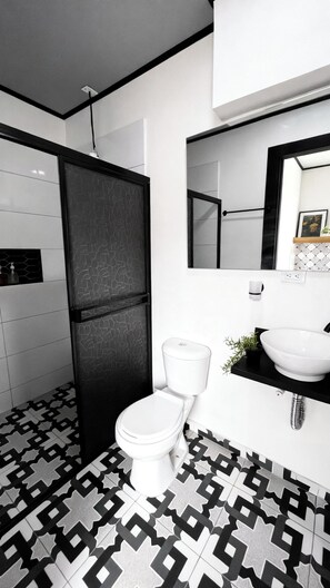 Une salle de bain moderne avec des toilettes, un lavabo et un miroir. Le sol est recouvert d’un motif géométrique noir et blanc.