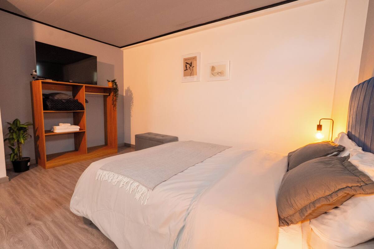 Une chambre à coucher avec un lit, une armoire en bois, une petite table et un téléviseur fixé au mur.