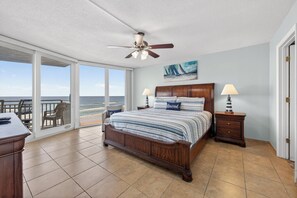 Ein Schlafzimmer mit einem großen Bett, einem Deckenventilator, Meerblick und einem Balkon mit Sitzgelegenheiten.