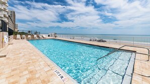 A swimming pool with a 3ft. in depth sign, surrounded by a tiled deck and a railing, overlooking a beach and ocean. - Coastal Daydream At White Surf (Daytona Beach)