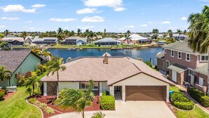A residential area with houses, a body of water, and a well-maintained lawn. - Riverfront Escape with Pool, Tiki Hut & Gulf Access Fun - Villa Kai Malie - Roelens (Cape Coral)