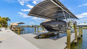 A boat docked at a pier with a covered area, a thatched-roof structure, and a clear view of the water. - Riverfront Escape with Pool, Tiki Hut & Gulf Access Fun - Villa Kai Malie - Roelens (Cape Coral)
