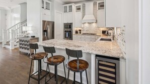 A modern kitchen with white cabinetry, a granite countertop, and a stainless steel refrigerator. - Edge of Rosemary Beach + 1 Minute Walk to Beach | Pool, Putting Green, Carriage House (Rosemary Beach)