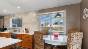 A modern kitchen with marble countertops, wicker chairs, and a dining table. - Spacious 4-bedroom Ranch Cape May Oasis Master Spa Hot Tub (Cape may)