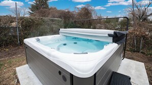 A hot tub with a metal frame, set on a concrete base, surrounded by a garden with trees and shrubs. - Spacious 4-bedroom Ranch Cape May Oasis Master Spa Hot Tub (Cape may)