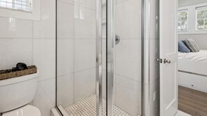 Un baño moderno con ducha de vidrio, inodoro y cama con almohadas.
