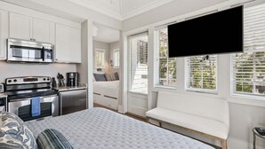Una habitación compacta con cama, televisión, kitchenette y ventana con persianas.