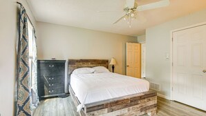A bedroom with a wooden headboard, a bed with white bedding, a ceiling fan, a dresser, and a door.