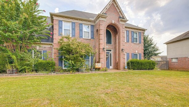 A two-story brick house with a prominent arched entryway and a well-maintained front yard.
