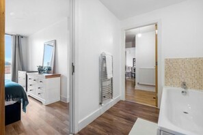 Egy modern hálószoba, amelyben található egy ágy, egy komód és egy nagy tükör. A hálószobából egy előszoba nyílik, amely egy fürdőszobába vezet, ahol kád és csempézett zuhanyzó található.