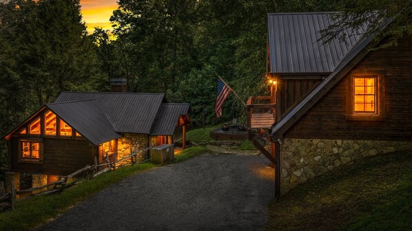 A row of log cabins with stone foundations, connected by a gravel path, set in a forested area. - Four Seasons Mountain Escape - Riverfront | Pet Friendly | Hot Tub (Blue Ridge)